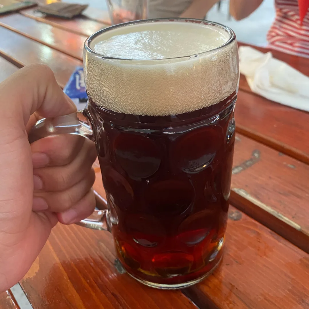 A Seidla of dark beer in a dimpled glass mug, held above a wooden table
